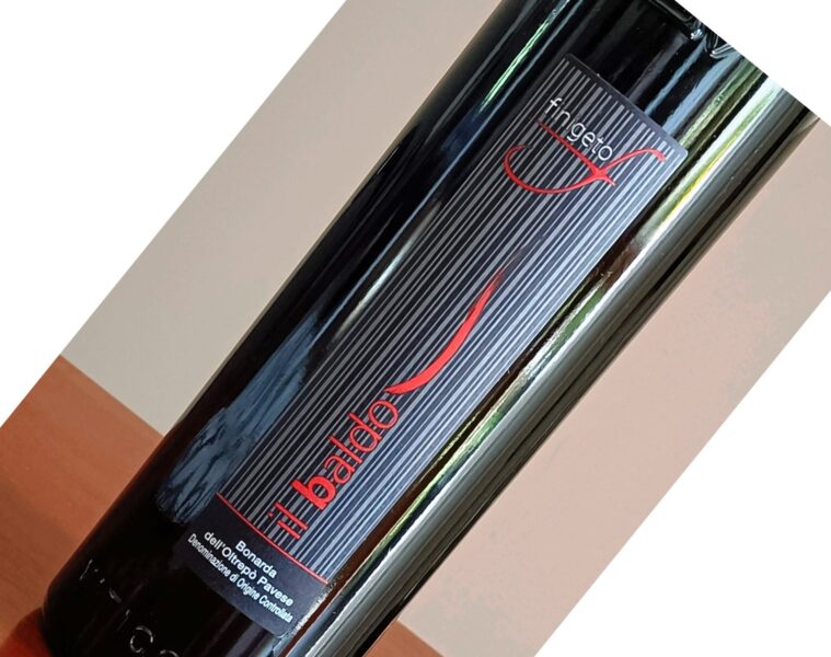 Close-up of a dark wine bottle with a vertically striped black label, a red logo, and the text 'Il Badardo' visible.