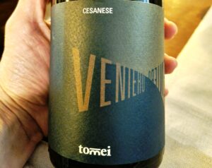 Close-up of a hand holding a dark bottle with a blue label, showing the word CESANESE.