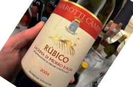 Close-up of a hand holding a wine bottle tilted, label reads Rubico with a red band and crest, vintage 2004.