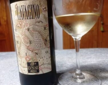 Wine bottle with a vintage map label reading 'CAVAGINO' beside a filled white wine glass on a gray countertop.