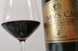 Close-up of a wine glass with red wine next to a gold-labeled wine bottle on the right.