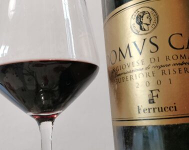 Close-up of a wine glass with red wine next to a gold-labeled wine bottle on the right.