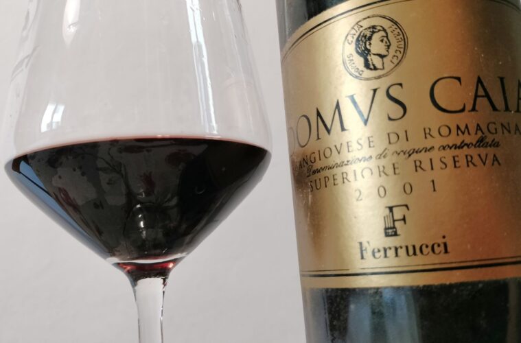 Close-up of a wine glass with red wine next to a gold-labeled wine bottle on the right.
