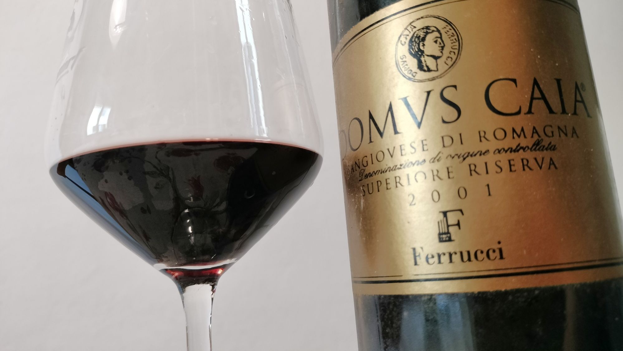 Close-up of a wine glass with red wine next to a gold-labeled wine bottle on the right.