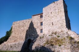 Stone fortress on a hill under a clear blue sky; a tall wall casts a dark shadow across the lower stones.