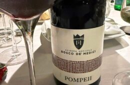 Wine bottle with label reading Bosco De Medici Pompeii on a dining table with wine glasses nearby.