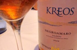 Wine glass beside a bottle labeled KREOS Negroamaro Salento 2024, a pale rosé wine visible in the glass.