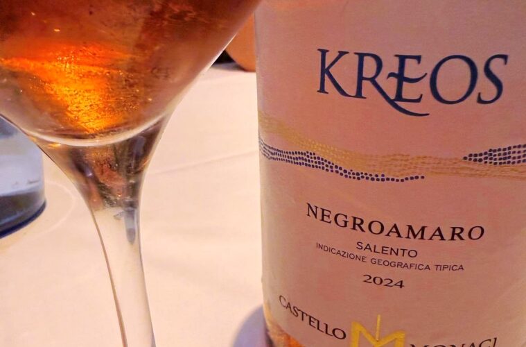 Wine glass beside a bottle labeled KREOS Negroamaro Salento 2024, a pale rosé wine visible in the glass.