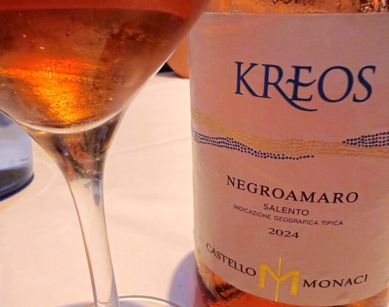 Wine glass beside a bottle labeled KREOS Negroamaro Salento 2024, a pale rosé wine visible in the glass.
