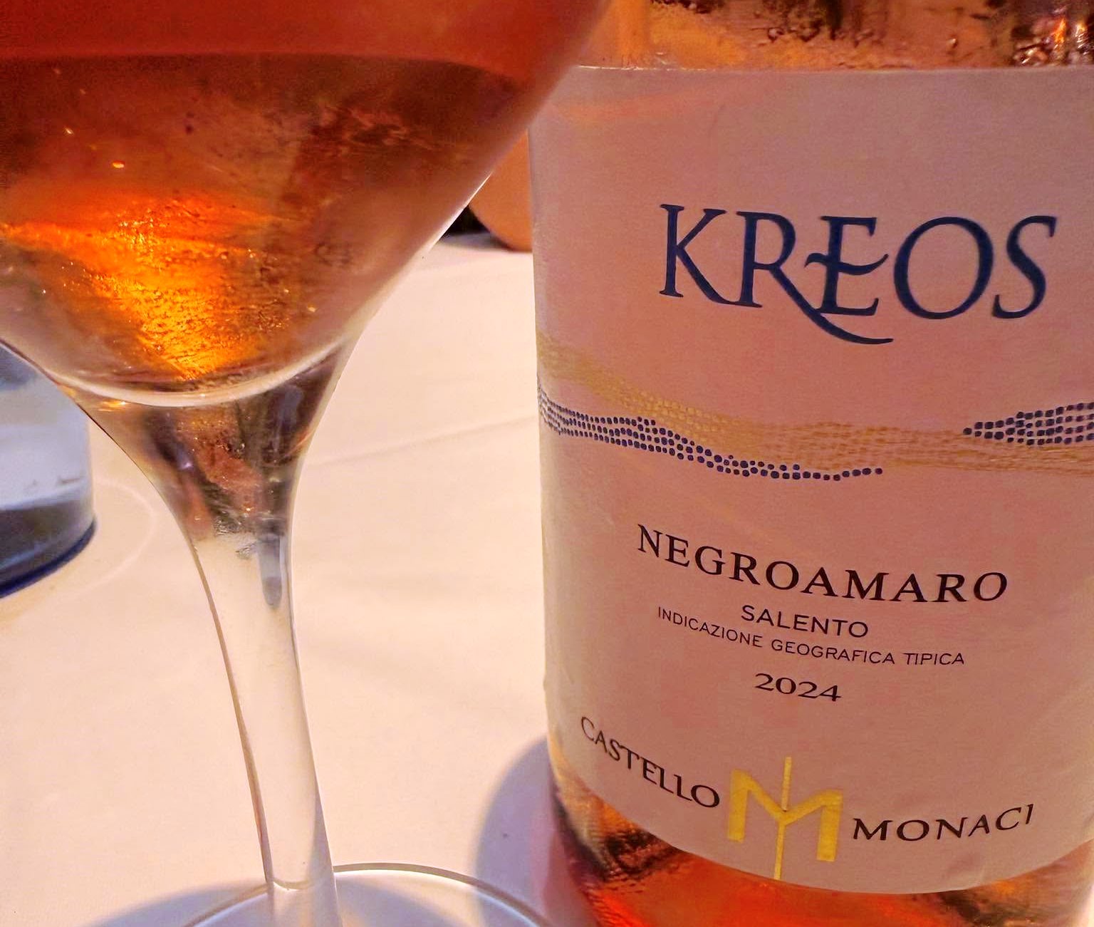 Wine glass beside a bottle labeled KREOS Negroamaro Salento 2024, a pale rosé wine visible in the glass.