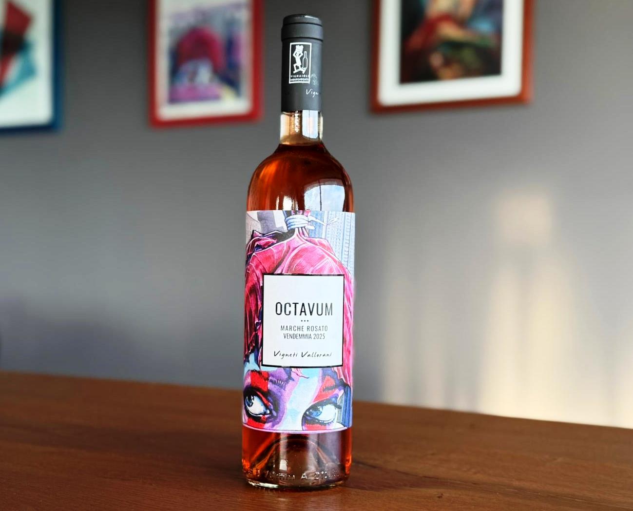 Rosé wine bottle on a wooden table with a colorful label reading 'OCTAVUM' and artwork in the background.