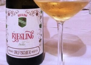 Bottle of Riesling wine beside a filled wine glass on a white tablecloth.
