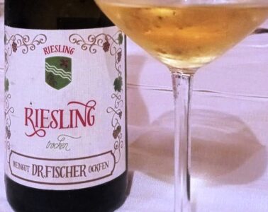 Bottle of Riesling wine beside a filled wine glass on a white tablecloth.
