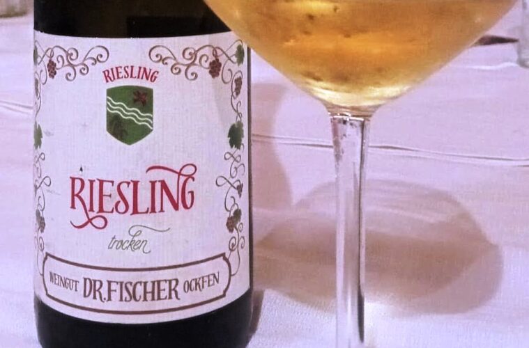 Bottle of Riesling wine beside a filled wine glass on a white tablecloth.