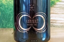Close-up of a dark wine bottle with an ornate gold circular design and decorative filigree, centered on the label within a glossy finish.