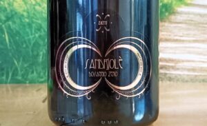 Close-up of a dark wine bottle with an ornate gold circular design and decorative filigree, centered on the label within a glossy finish.