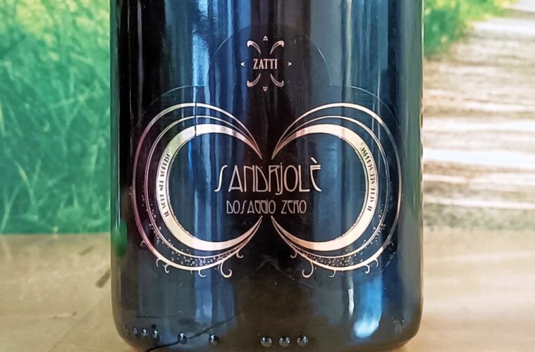 Close-up of a dark wine bottle with an ornate gold circular design and decorative filigree, centered on the label within a glossy finish.