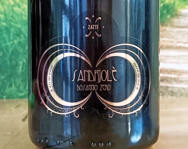 Close-up of a dark wine bottle with an ornate gold circular design and decorative filigree, centered on the label within a glossy finish.