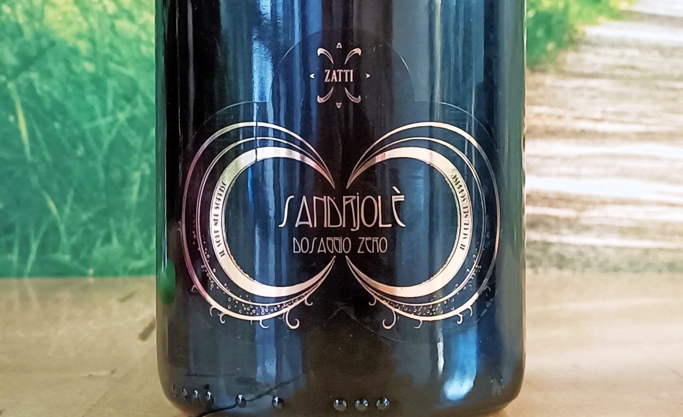 Close-up of a dark wine bottle with an ornate gold circular design and decorative filigree, centered on the label within a glossy finish.