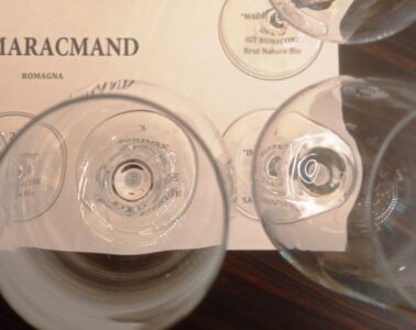 Top-down view of several empty wine glasses placed over a printed label that reads AMARACMAND ROMAGNA.