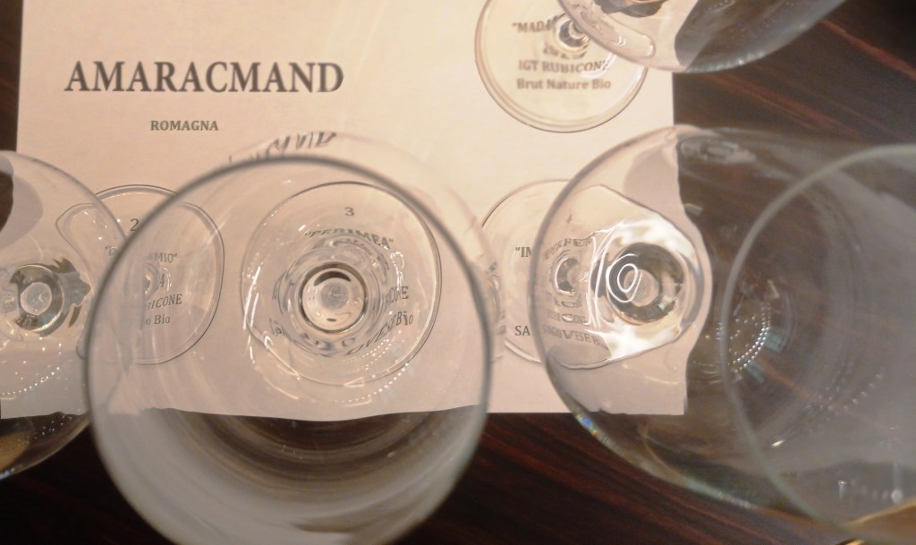 Top-down view of several empty wine glasses placed over a printed label that reads AMARACMAND ROMAGNA.