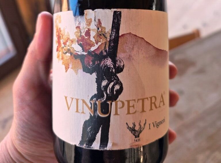 Wine bottle held by a hand, with a label showing an abstract tree and autumn leaves and vertical text.