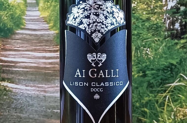Bottle of AI GALLI Lison Classico DOCG wine with a black label and white crest against a garden backdrop; ornate crown at the top and a shield-shaped label showing the text AI GALLI LISON CLASSICO DOCG.