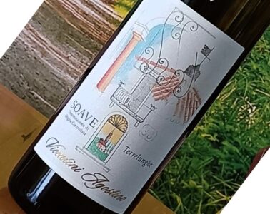 Bottle of wine on a wooden table with a decorative label featuring architectural motifs and the word 'Soave' (tilted in the photo).