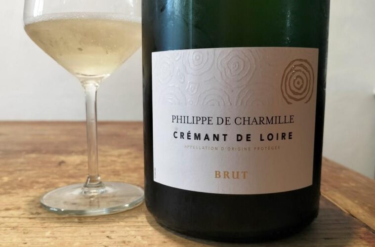 Bottle of Philippe de Charmille Crémant de Loire Brut next to a wine glass on a wooden table.