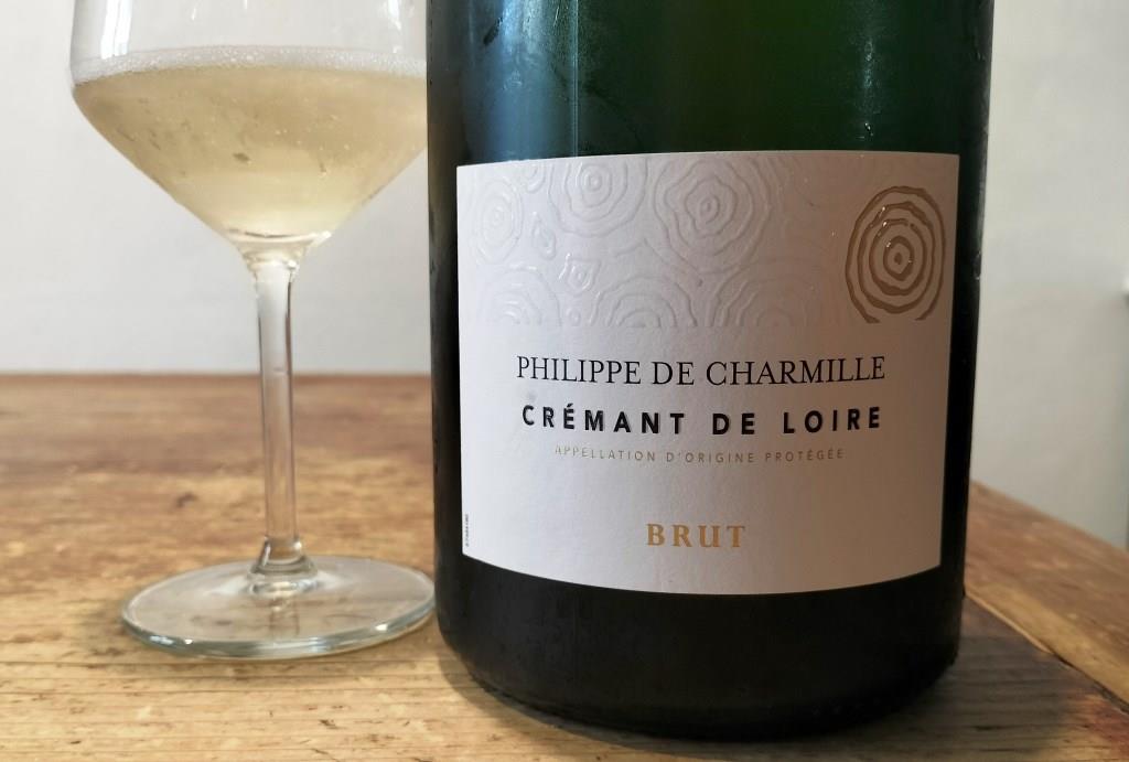 Bottle of Philippe de Charmille Crémant de Loire Brut next to a wine glass on a wooden table.