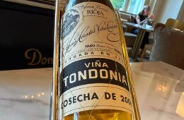 Close-up of a wine bottle in a metal holder on a dining table, label reads Viña Tondonia Rioja.