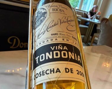 Close-up of a wine bottle in a metal holder on a dining table, label reads Viña Tondonia Rioja.