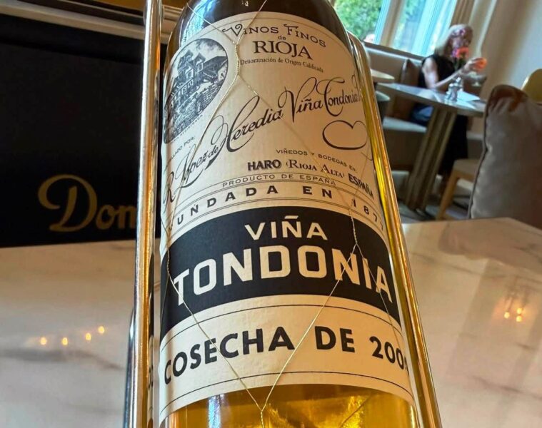 Close-up of a wine bottle in a metal holder on a dining table, label reads Viña Tondonia Rioja.