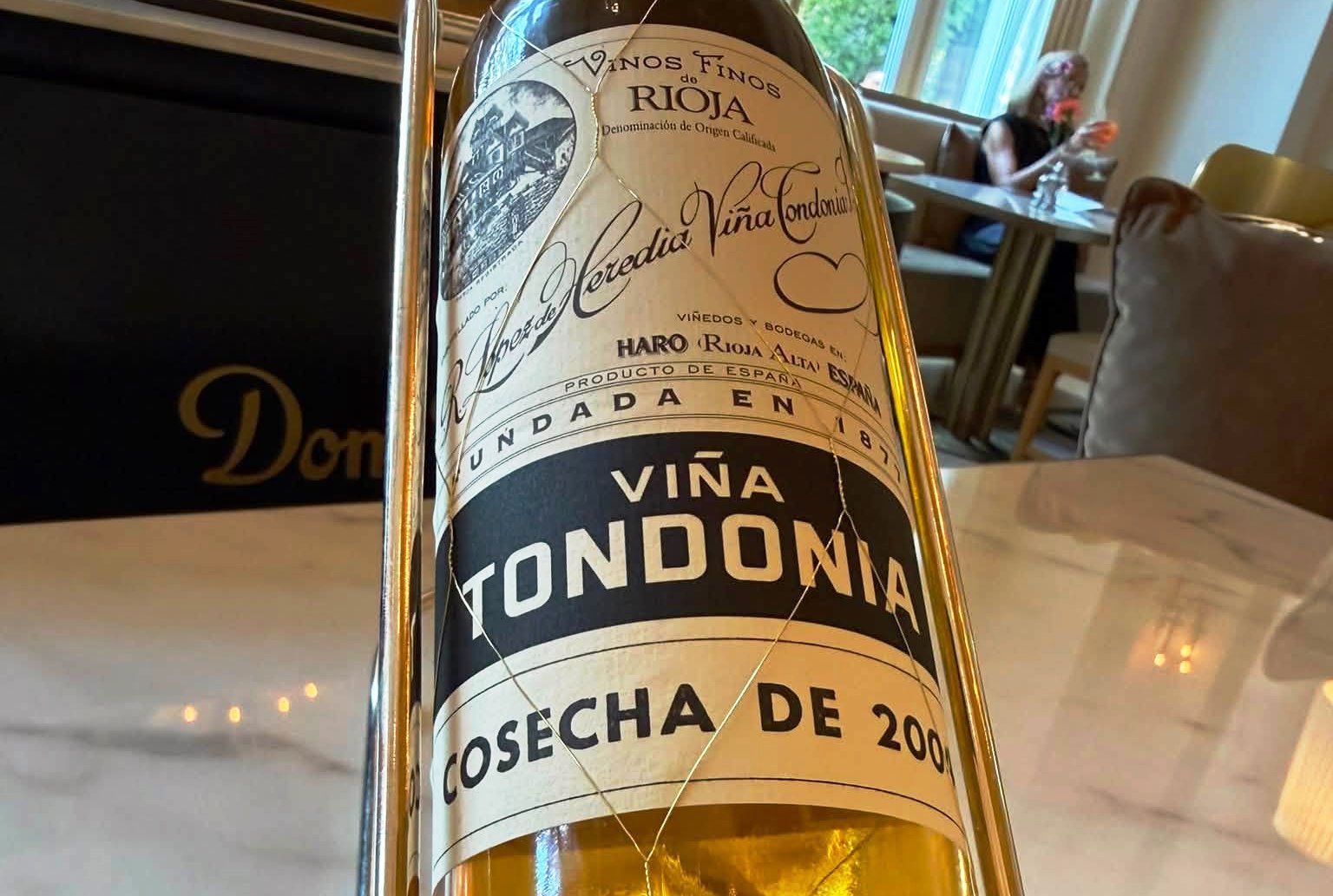 Close-up of a wine bottle in a metal holder on a dining table, label reads Viña Tondonia Rioja.