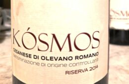 Close-up of a wine bottle label with the large word 'Kosmos' and smaller Italian origin text (Cesanese di Olevano Romano).