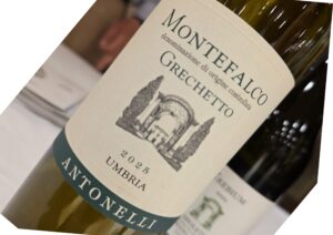 Close-up of a wine bottle on its side, cream label with teal border and a faint architectural illustration.