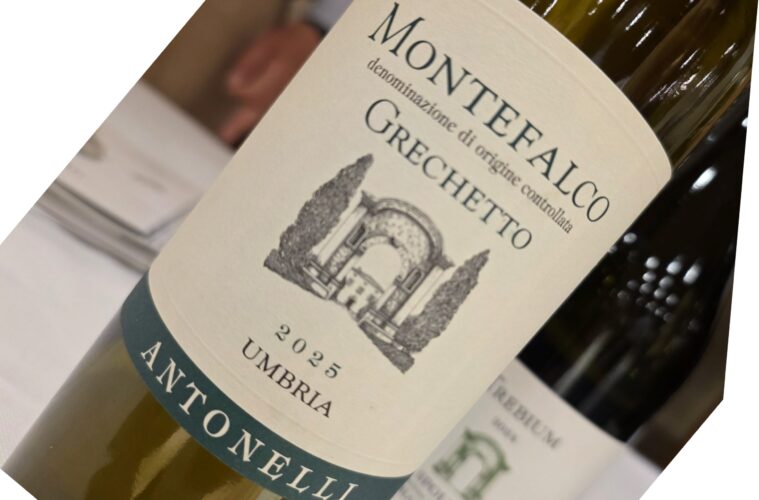Close-up of a wine bottle on its side, cream label with teal border and a faint architectural illustration.