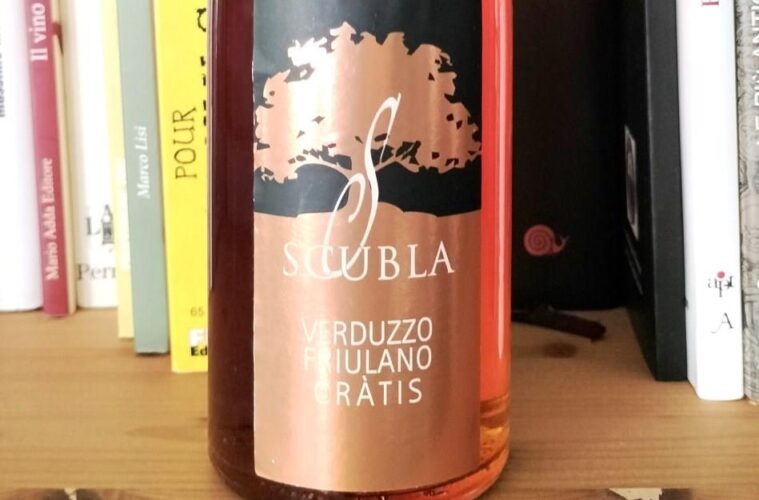 Wine bottle on a wooden shelf in front of books; copper label reads 'SCUBLA' with 'Verduzzo Friulano Gràtis'