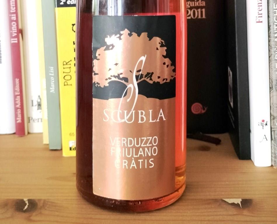 Wine bottle on a wooden shelf in front of books; copper label reads 'SCUBLA' with 'Verduzzo Friulano Gràtis'