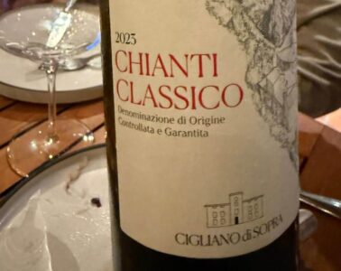 Close-up of a 2023 Chianti Classico wine bottle label with a hillside village illustration on the label, on a dining table with a glass nearby.