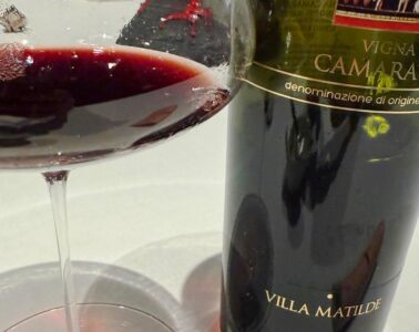Wine bottle labeled Villa Matilde, Vigna Camarato, gently poured red wine in a glass beside it on a white table.