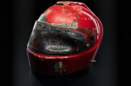 Close-up of a red racing helmet with a dirty, scratched visor against a dark background.