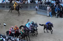 Jockeys in colorful silks race around a dirt track as a crowd watches from the stands.